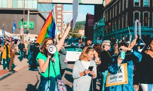 A vibrant protest with diverse participants holding flags and signs on a city street.