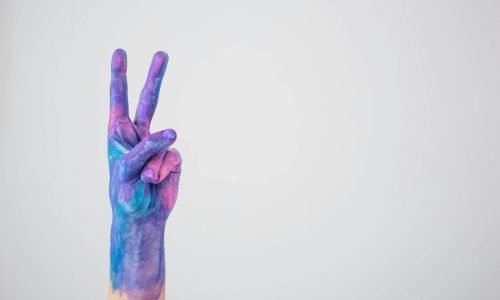 Vividly painted hand making a peace sign against a plain background.