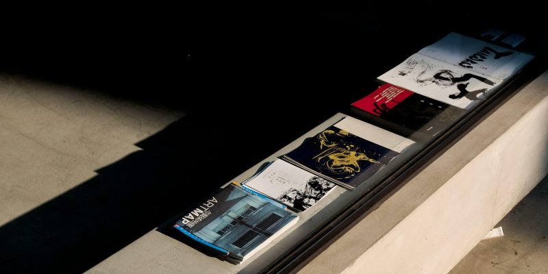 Art magazines and brochures on a sunlit concrete surface, highlighting shadow play and design.