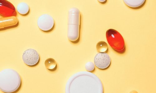 Colorful assortment of pills and capsules on a vibrant yellow background.