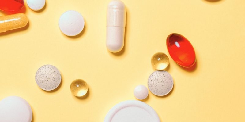 Colorful assortment of pills and capsules on a vibrant yellow background.