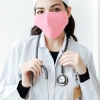 A doctor wearing a pink face mask and a stethoscope, symbolizing health and protection.